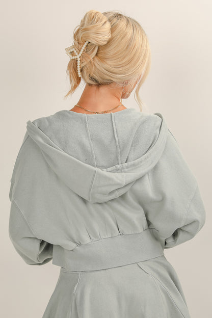 Person wearing a light gray hooded garment against a plain background