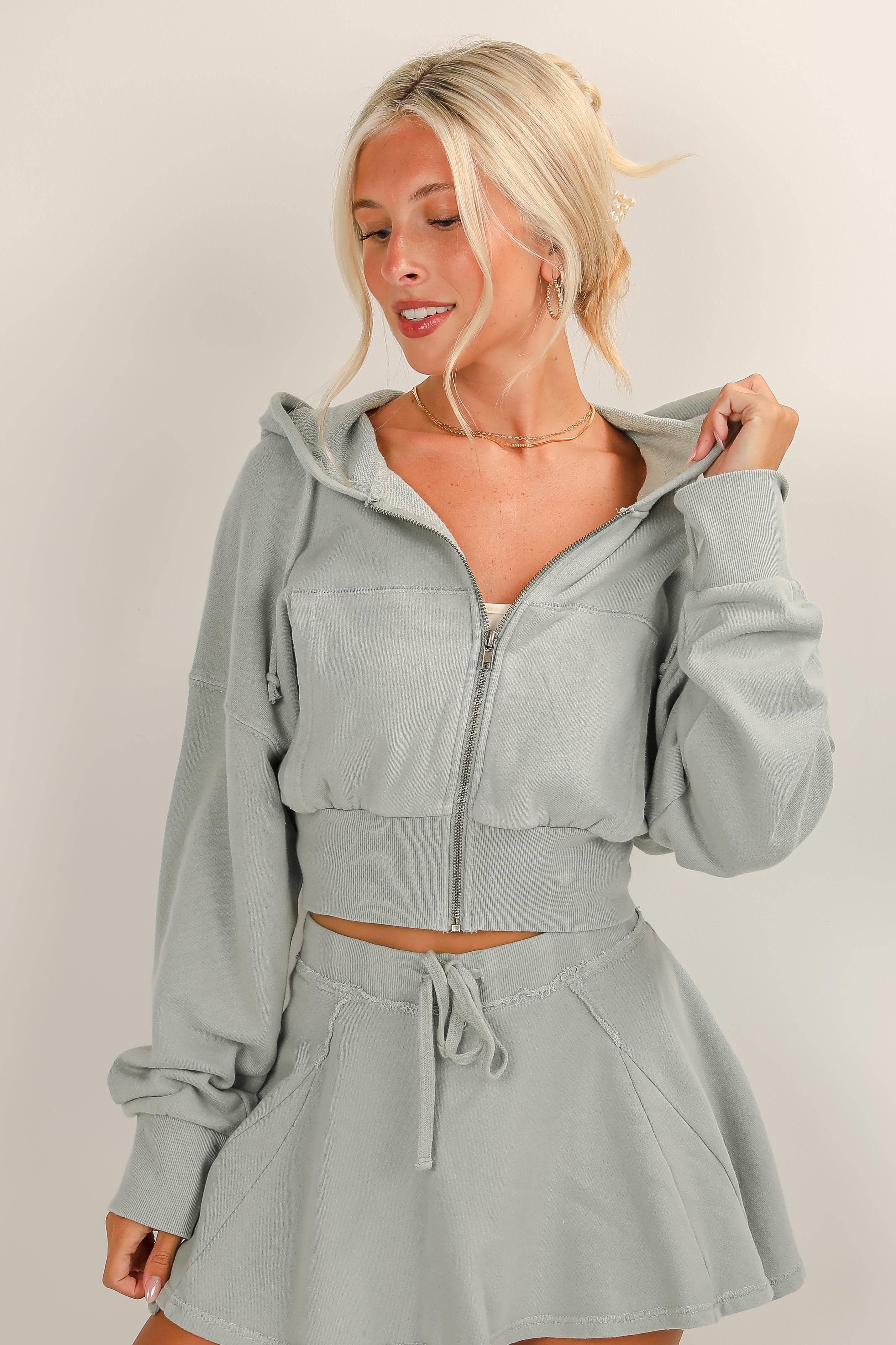 Woman wearing a light gray hoodie and skirt set against a plain background