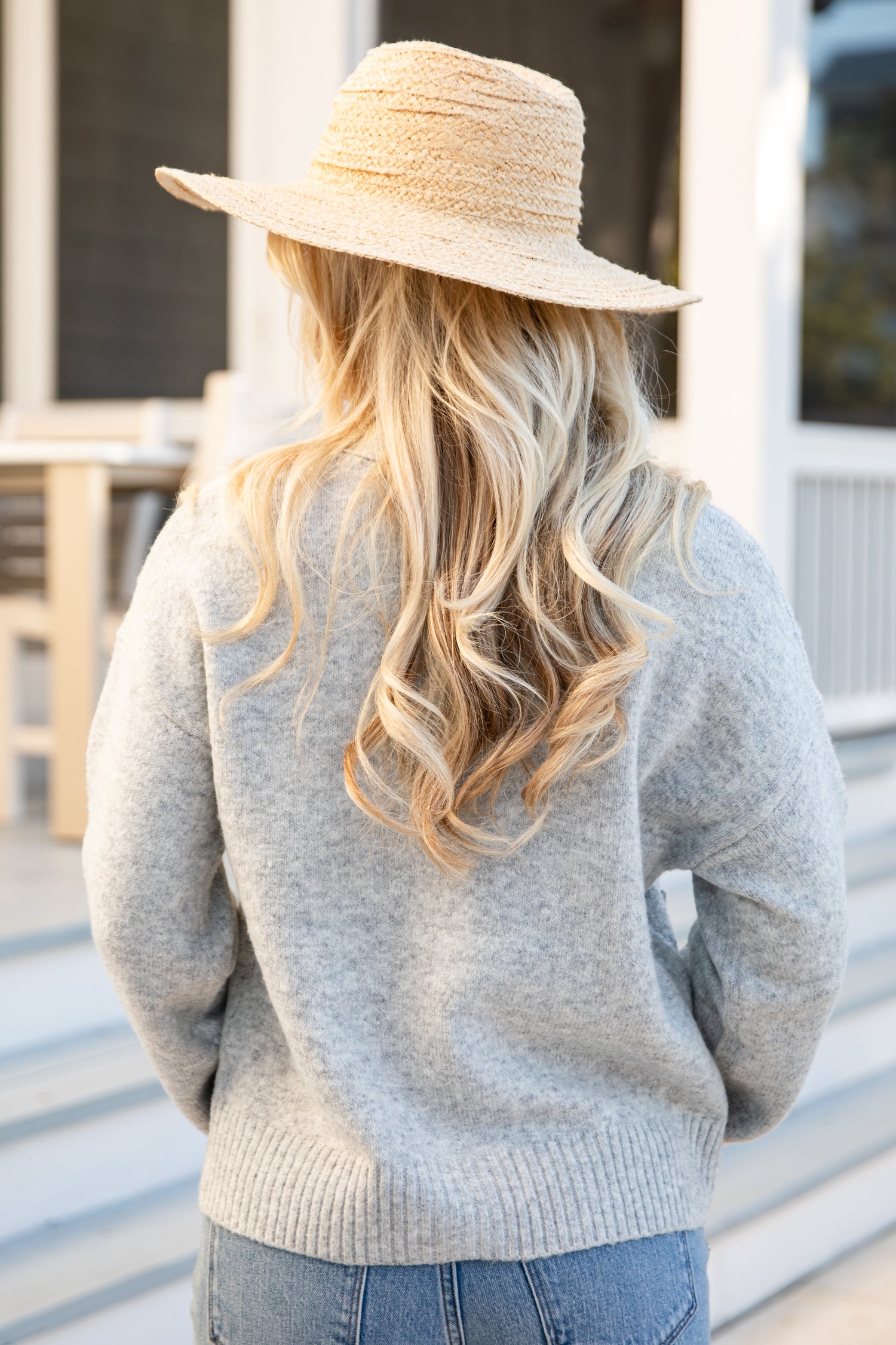 Person wearing a straw hat and gray sweater with long blonde hair.
