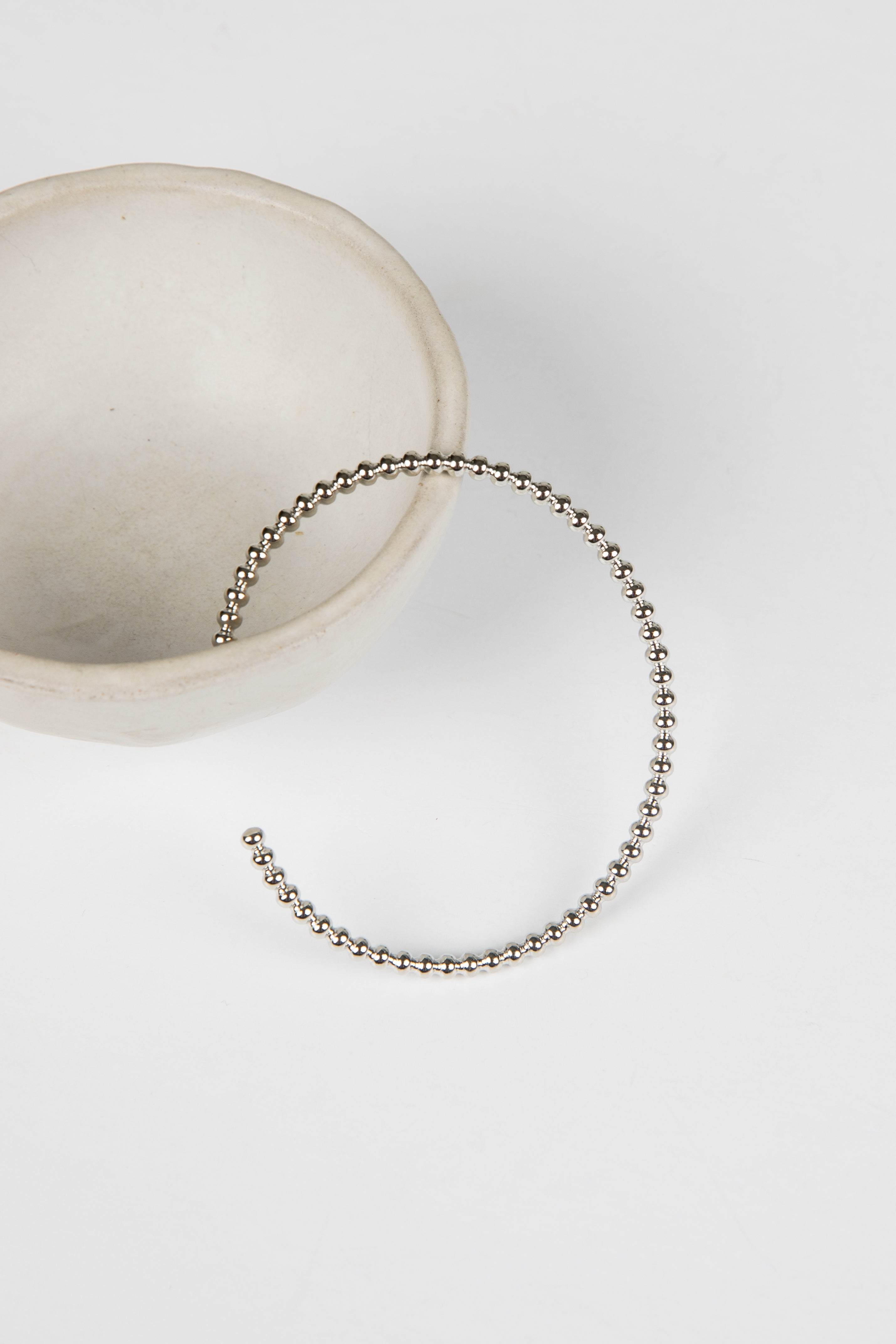 Silver beaded bracelet on a white surface with a neutral background