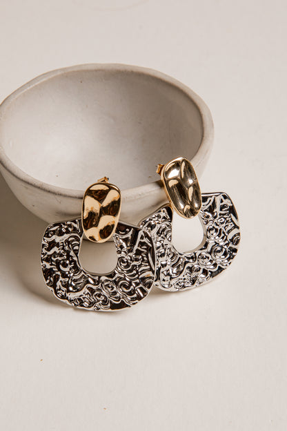 Pair of gold and silver hoop earrings on a white surface with a small white bowl.