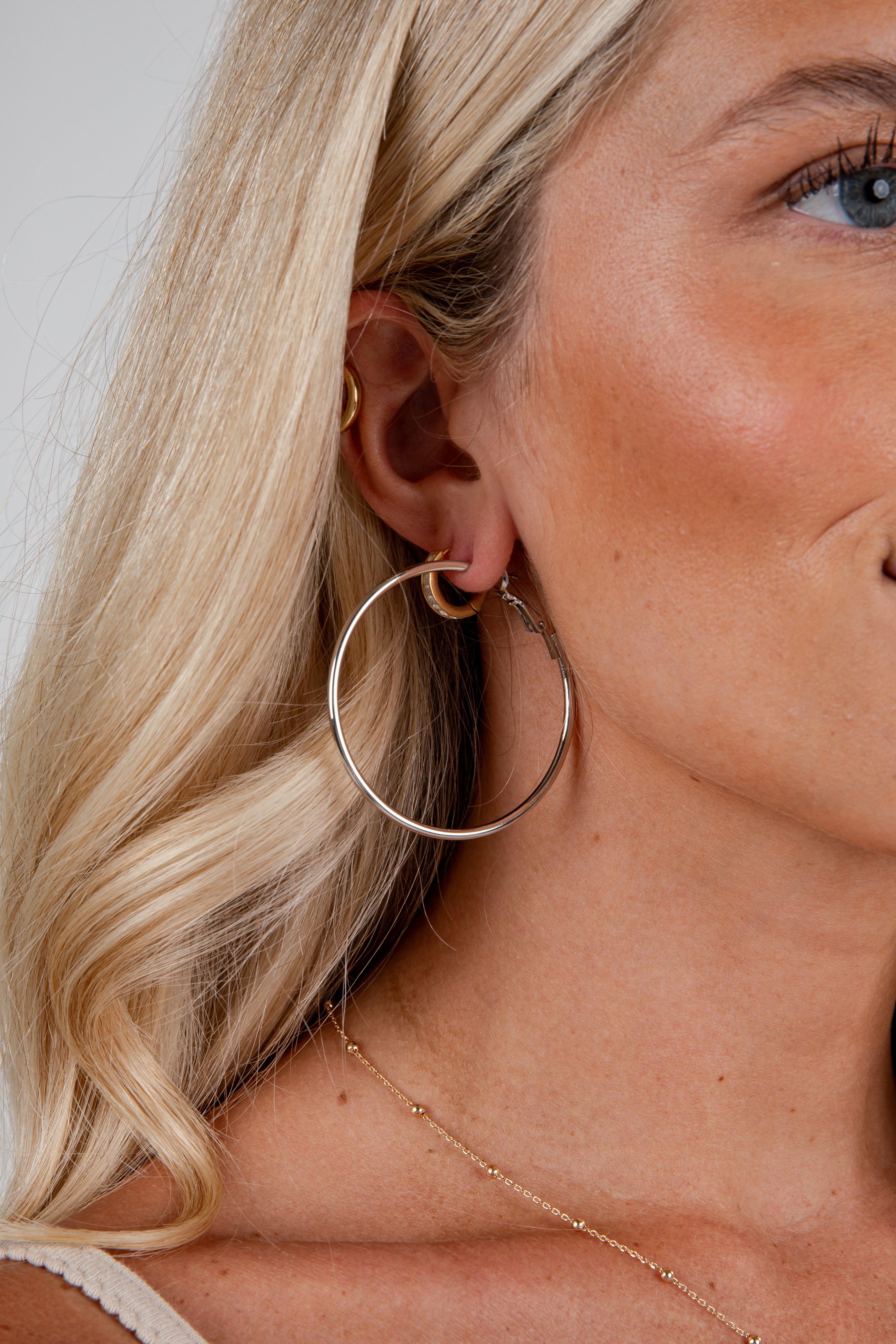 Close-up of a woman wearing gold hoop earrings with a neutral background