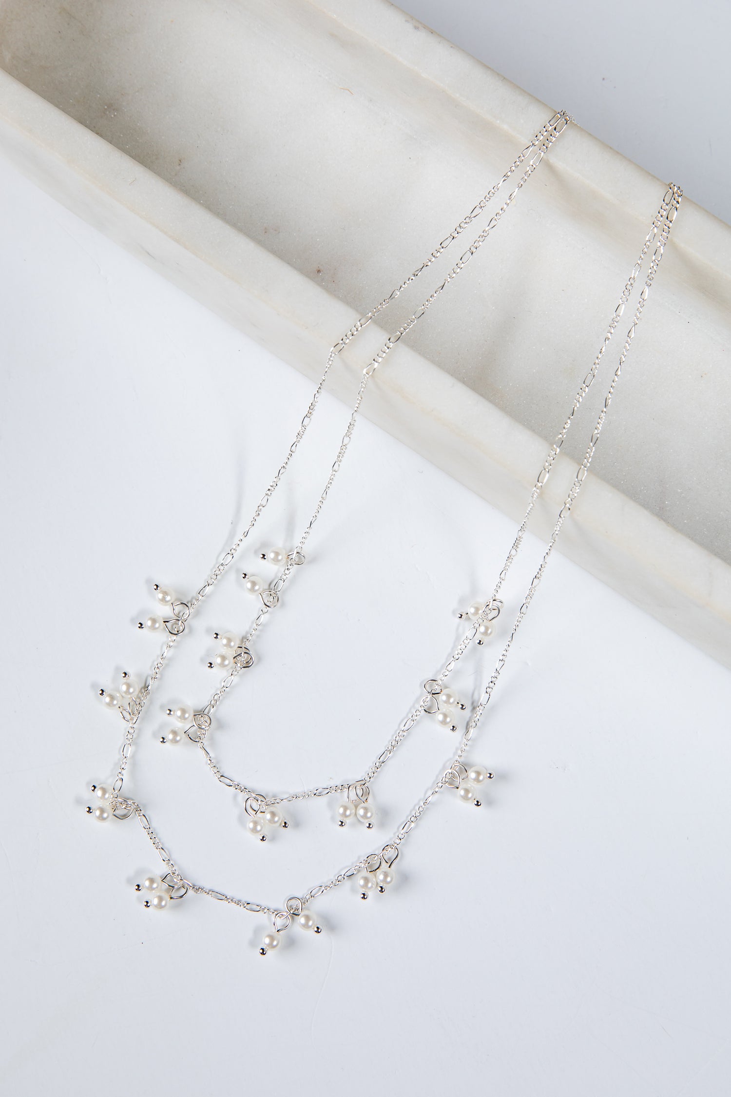 Silver necklace with small pearls on a white surface