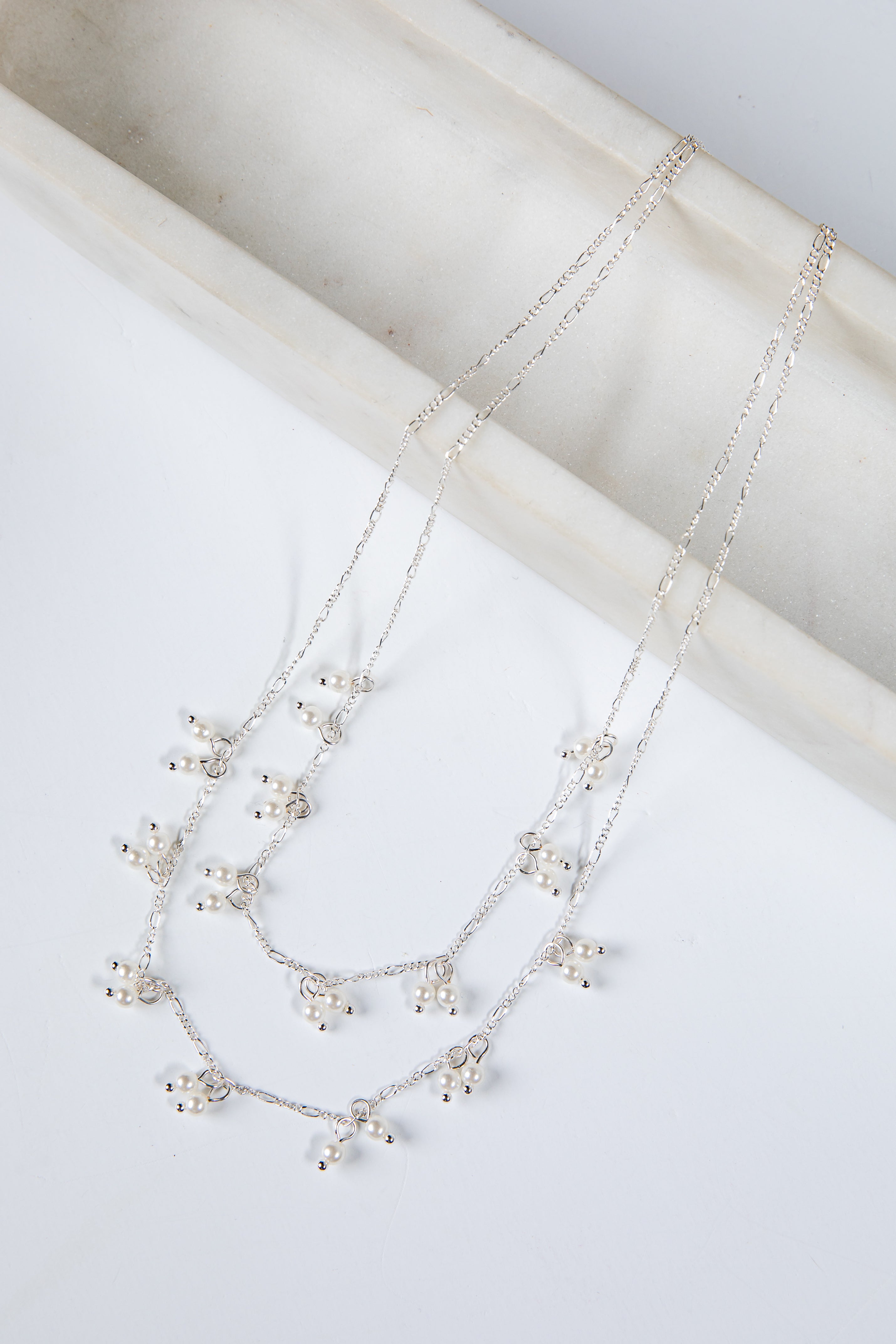 Silver necklace with small pearls on a white surface