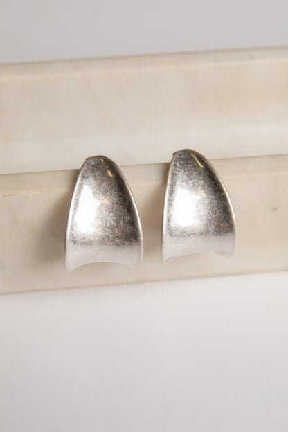 Pair of silver earrings on a light wooden stick against a white background