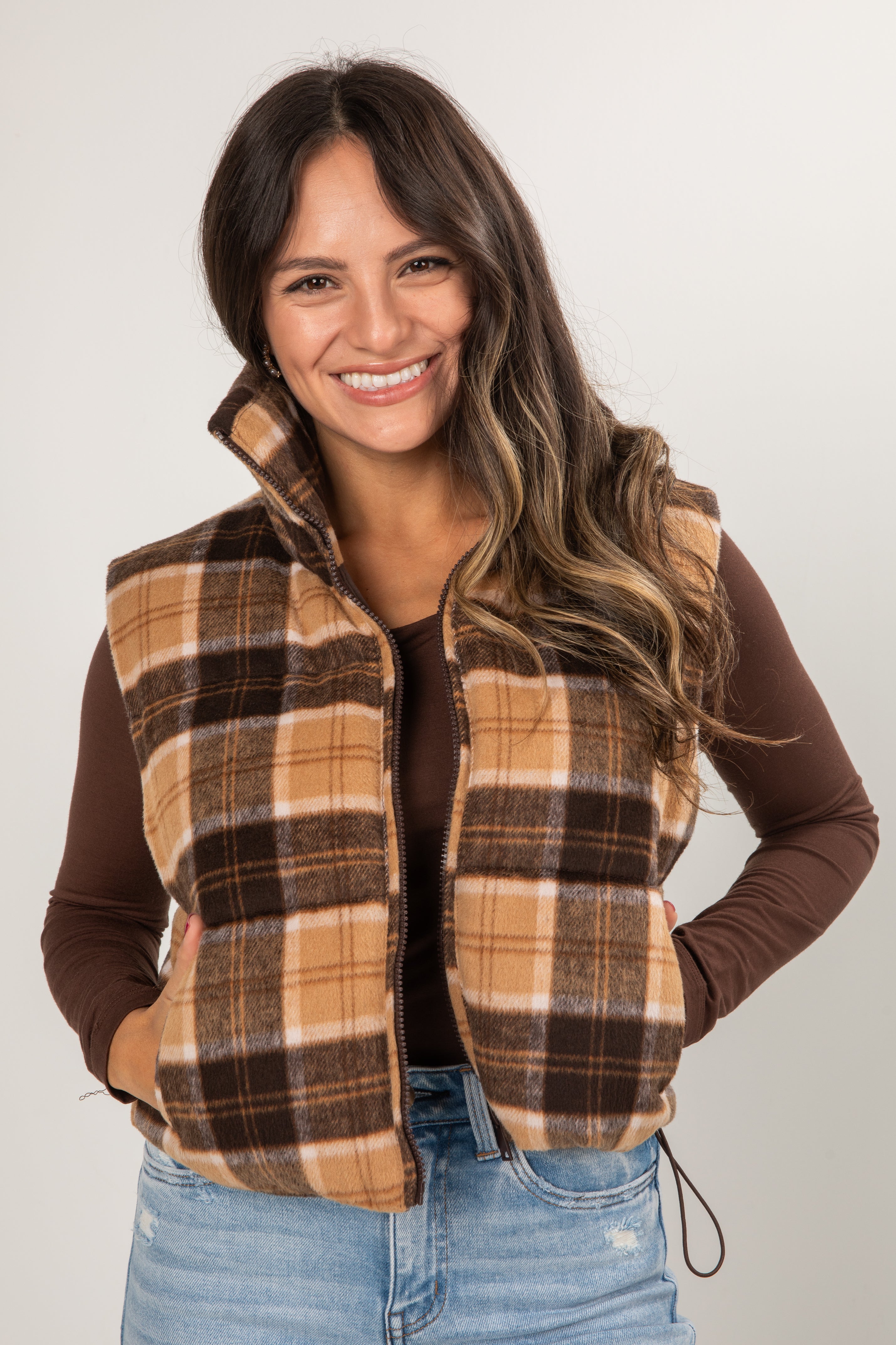 Woman wearing a plaid vest over a brown long-sleeve shirt with a white background