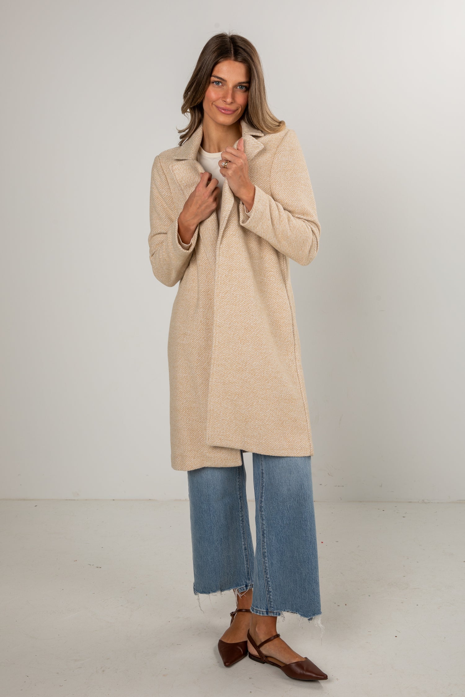 Woman wearing a beige coat and blue jeans on a white background