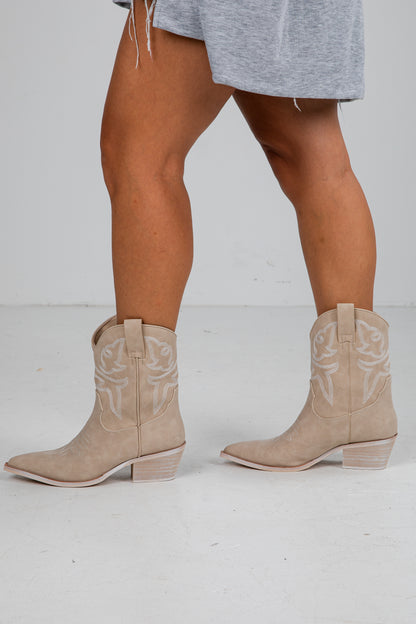 Beige cowboy boots worn with a gray dress on a white background
