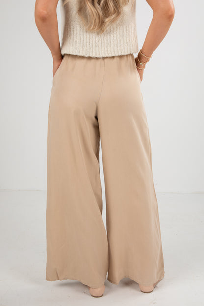 Person wearing beige wide-leg pants and a white top on a plain background