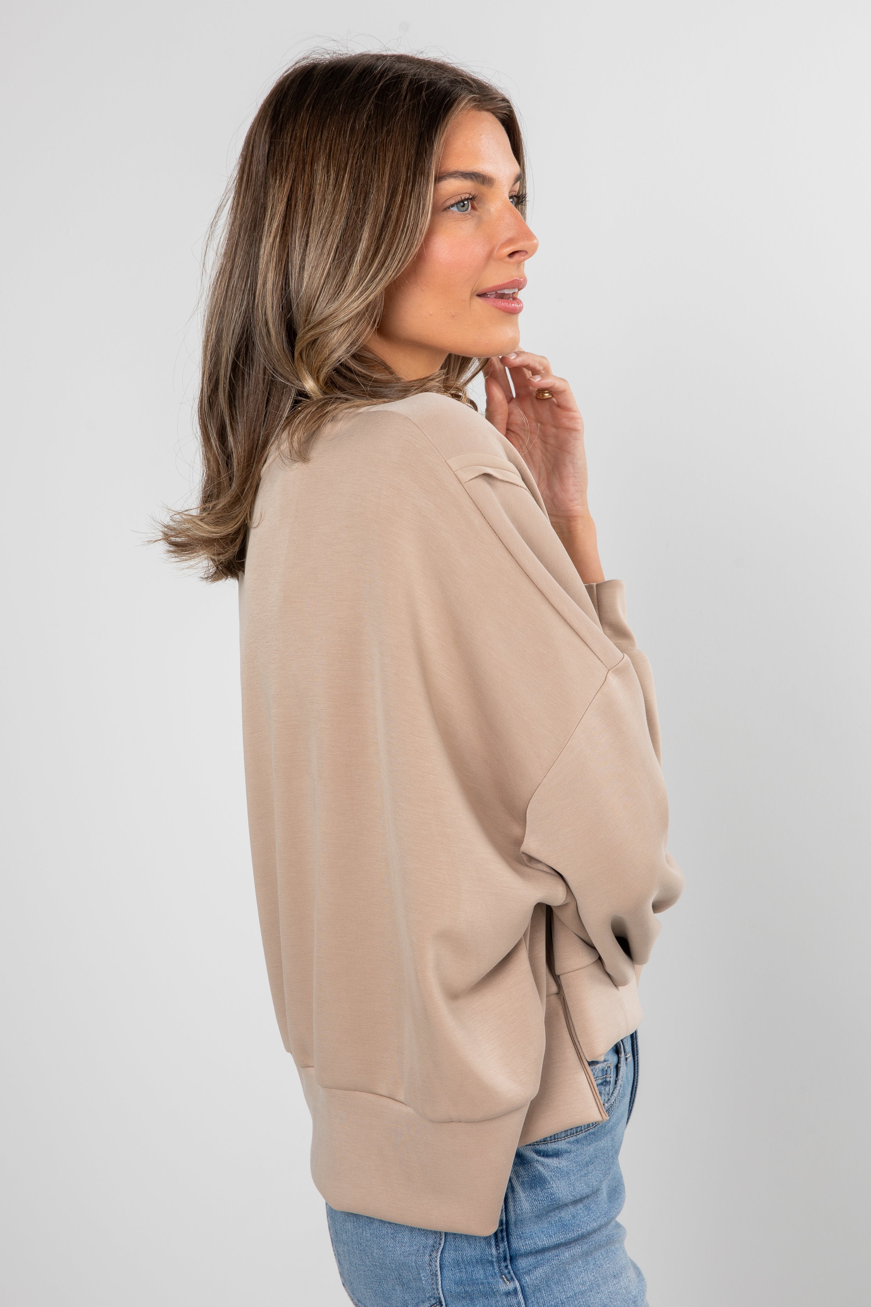 Woman wearing a beige sweater and blue jeans on a white background