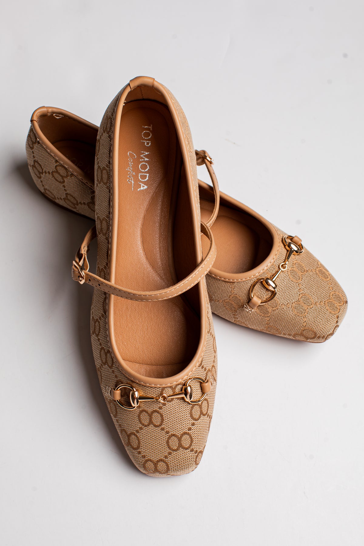 A pair of beige monogram ballet flats with gold-tone horsebit details and ankle straps, displayed on a light gray background. The brand &