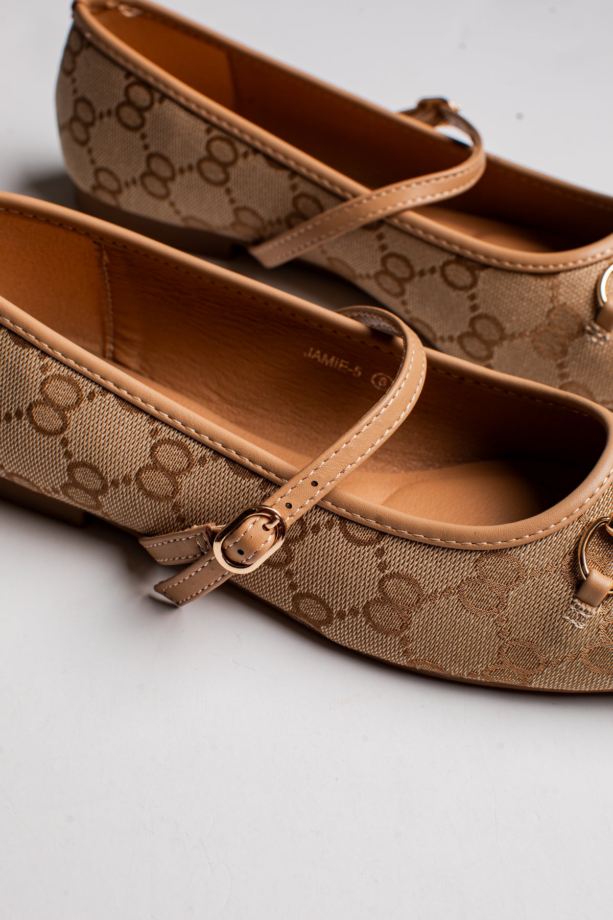 A pair of Gucci flat shoes in the classic GG Supreme canvas, featuring a tan and brown monogram pattern, adjustable strap with gold-tone buckles, and a small gold-tone ring detail on the toe.