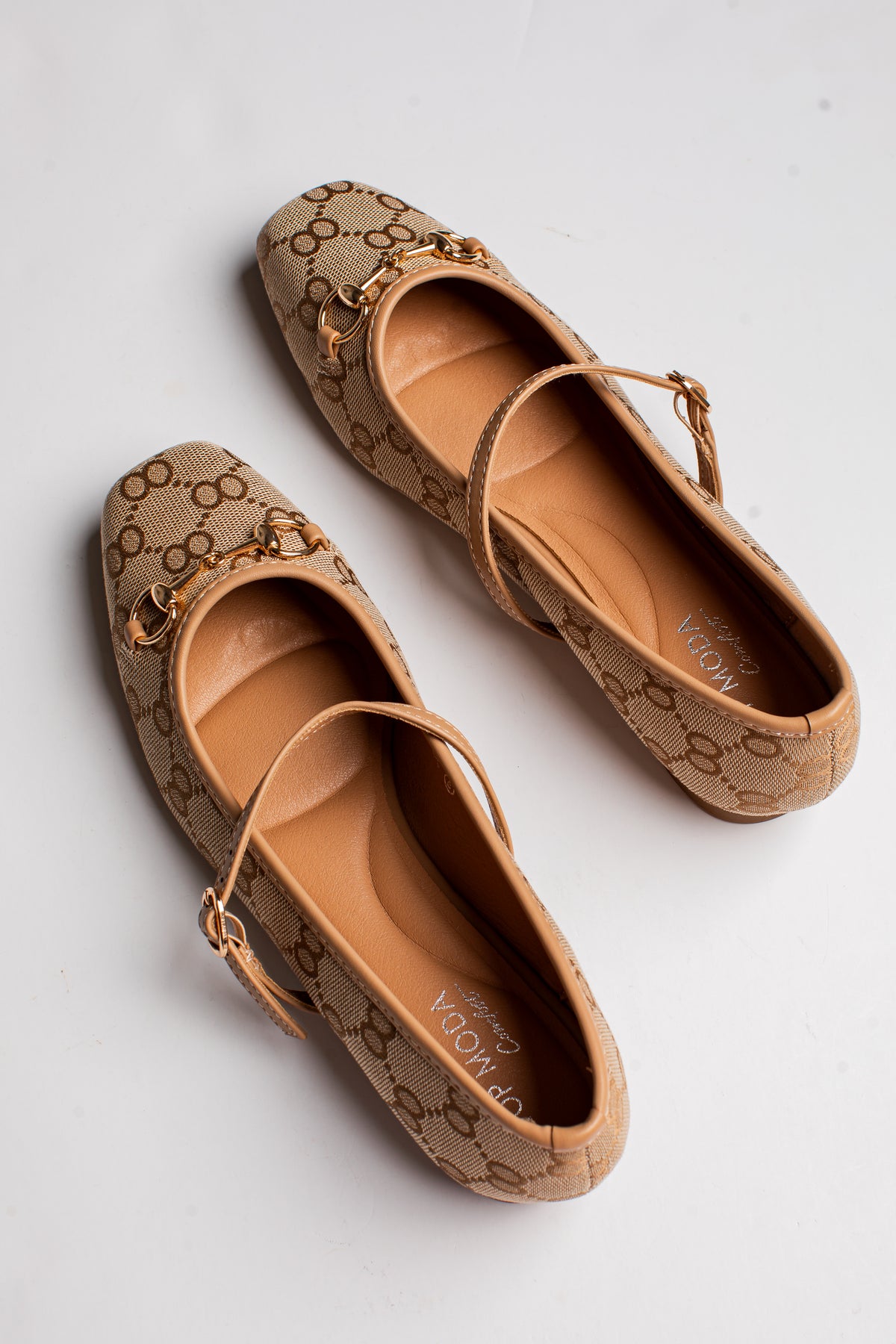 A pair of Gucci Mary Jane flats in the classic GG Supreme canvas, featuring a tan and brown monogram pattern with gold-tone horsebit details and ankle straps, photographed on a light gray background.