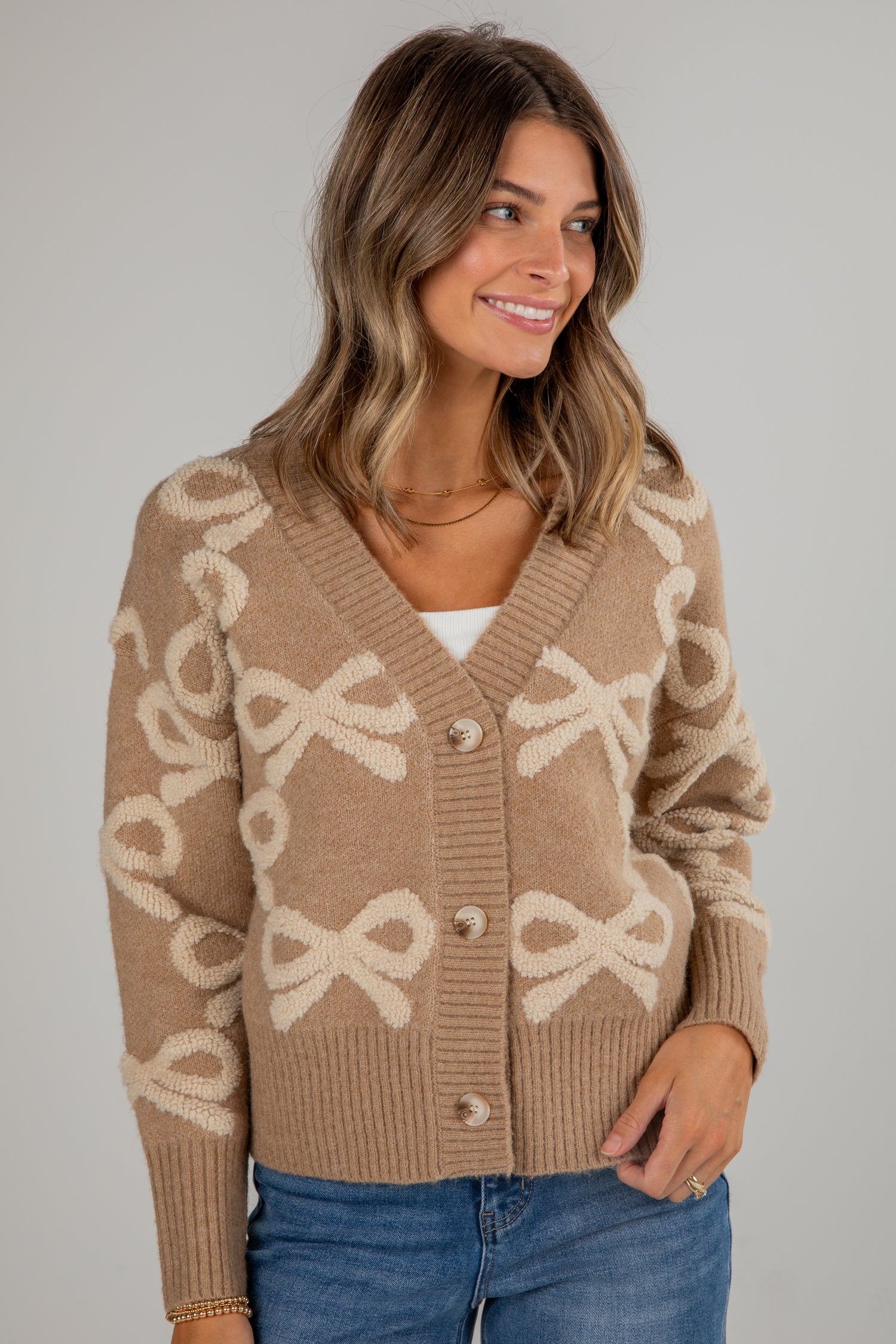 Woman wearing a beige cardigan with bow pattern on a plain background