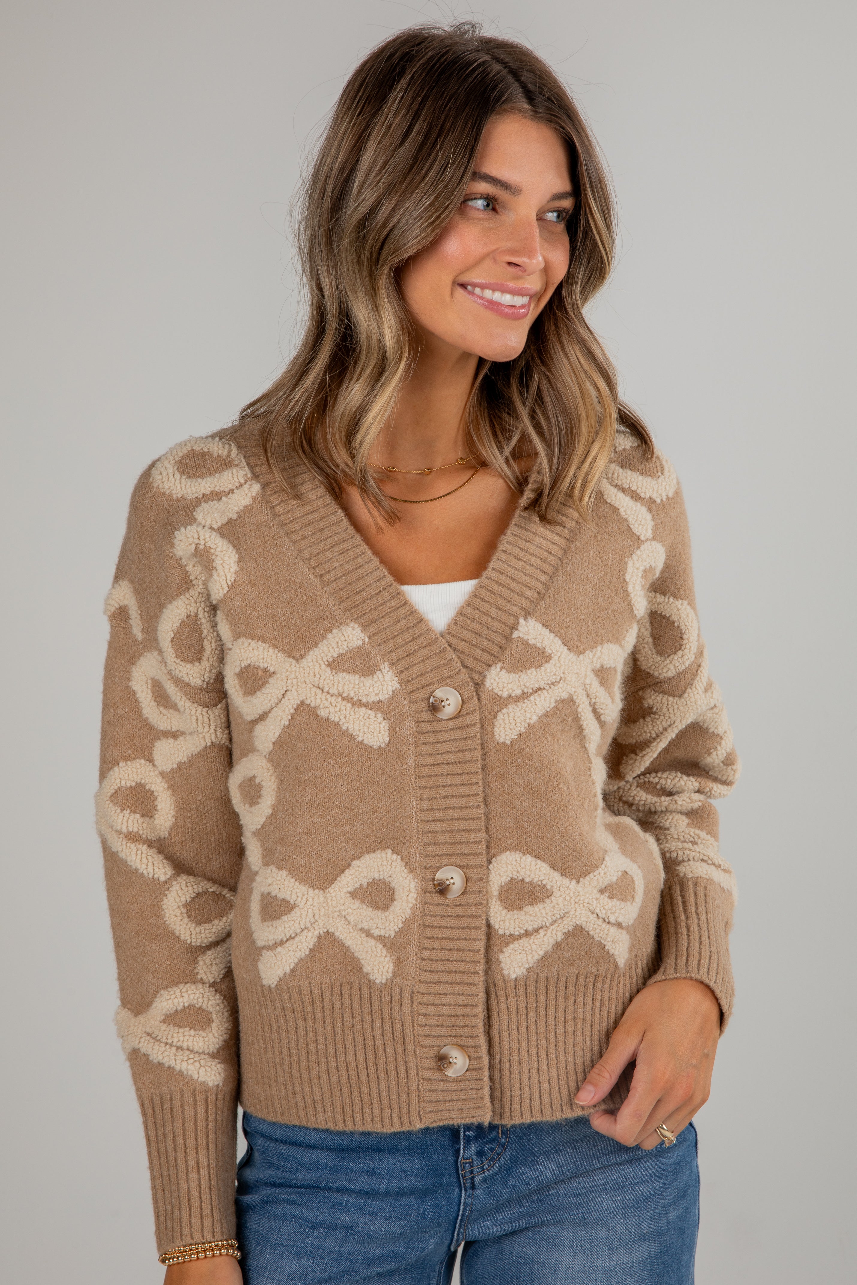 Woman wearing a beige cardigan with bow pattern on a plain background