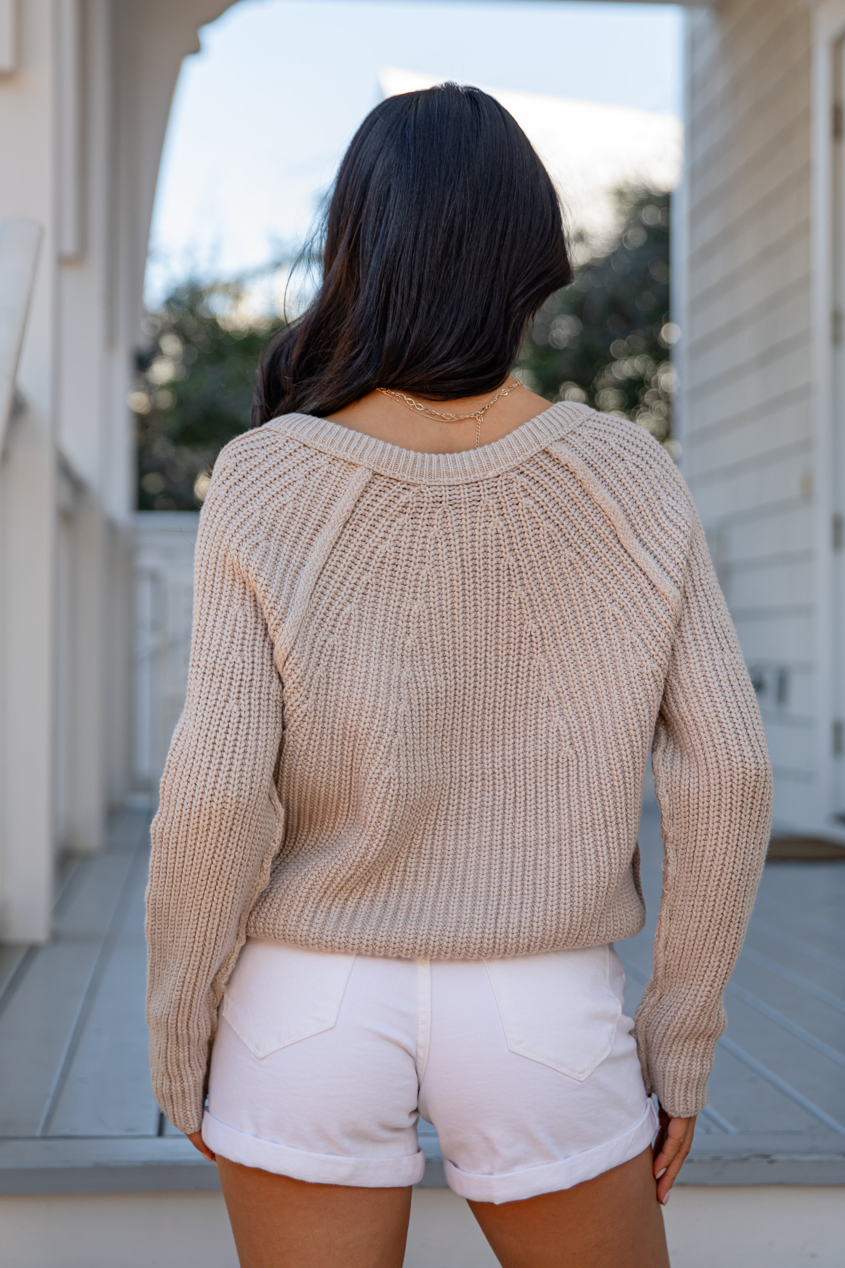 Person wearing a beige sweater and white shorts standing outdoors.