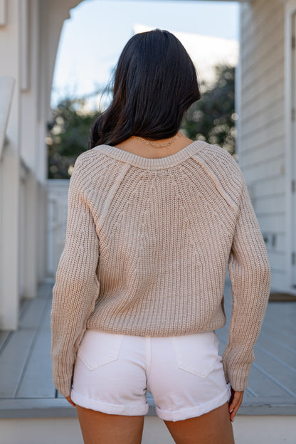 Person wearing a beige sweater and white shorts standing outdoors.