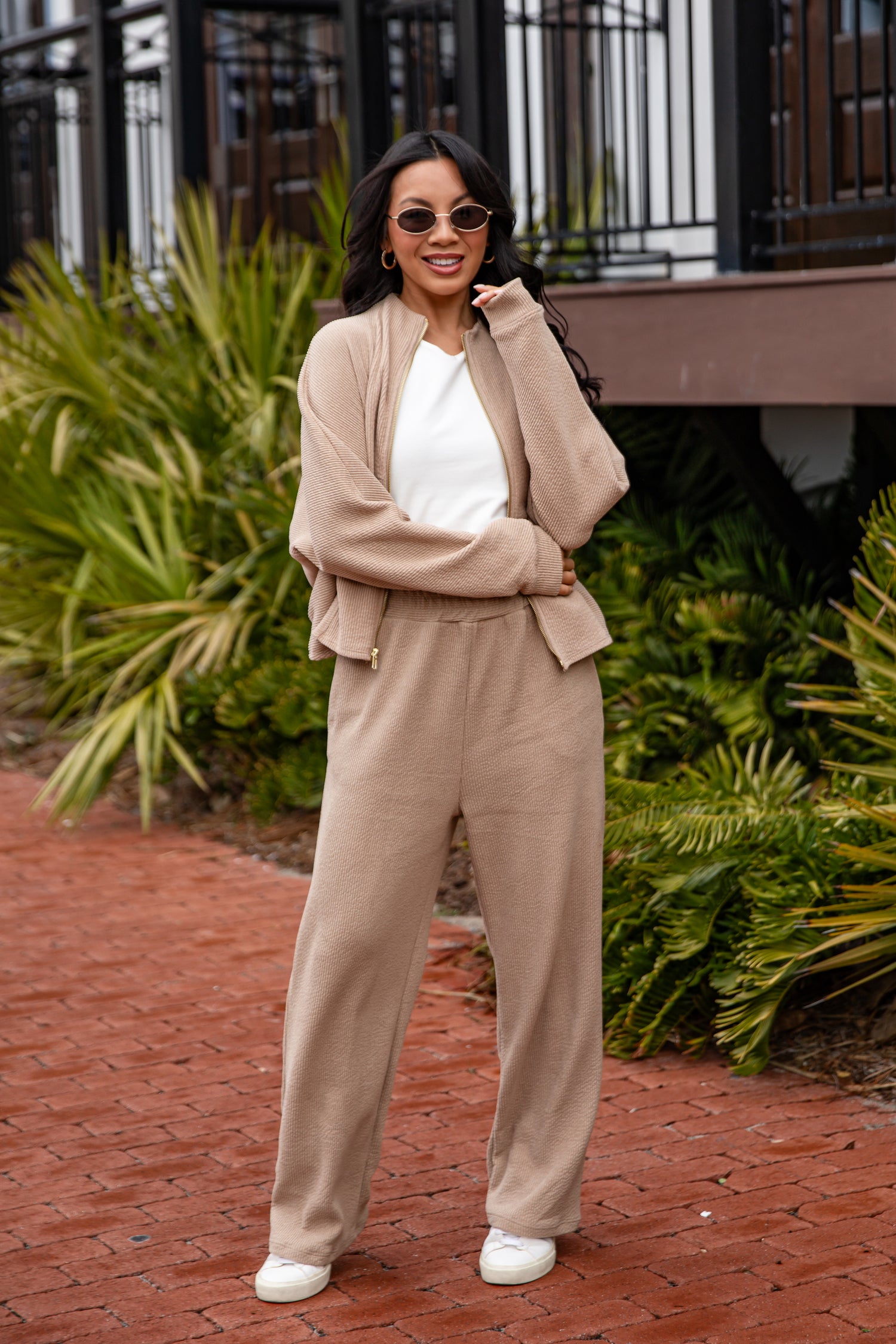 Woman in beige outfit standing outdoors with greenery in the background