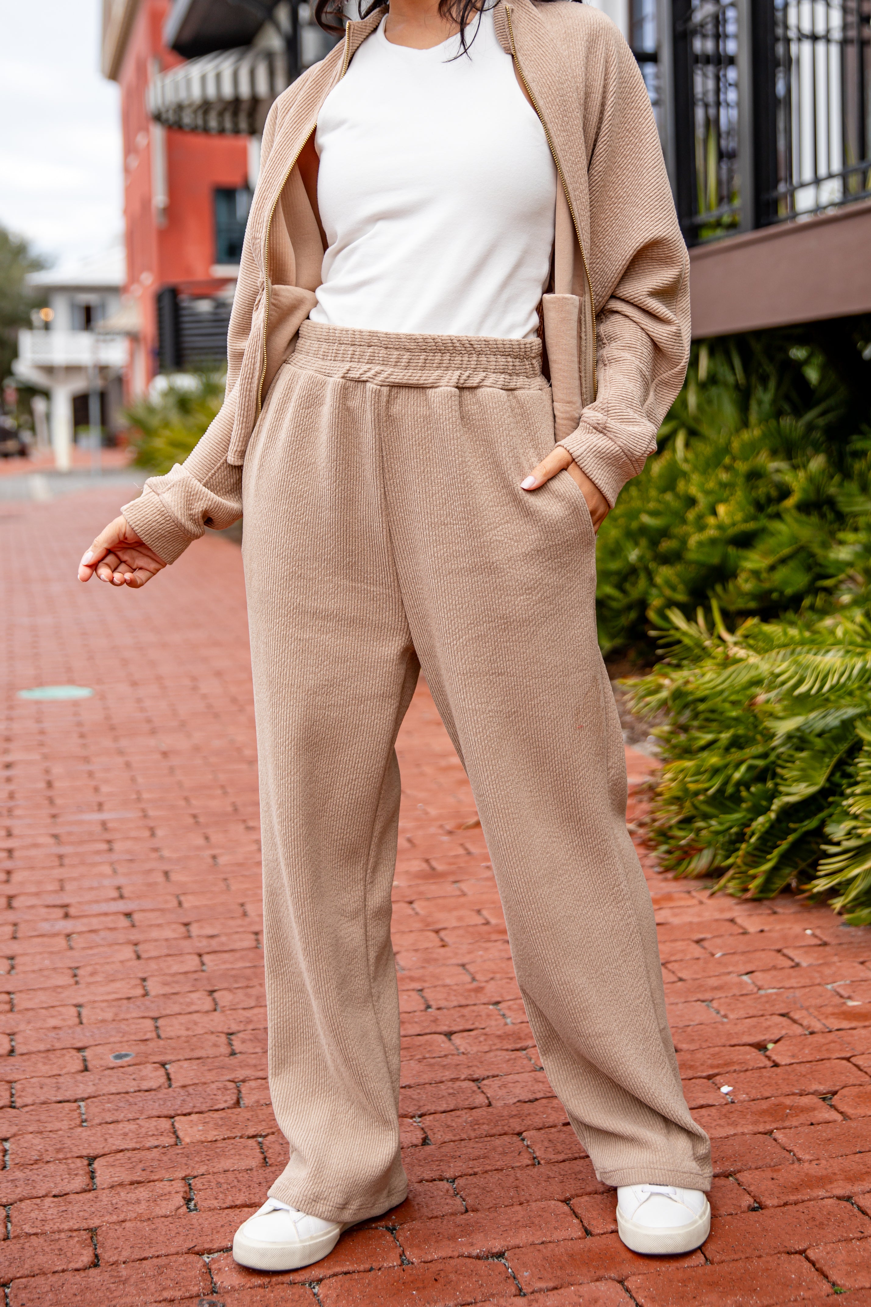 Person wearing a beige cardigan and pants with a white top on a brick sidewalk.