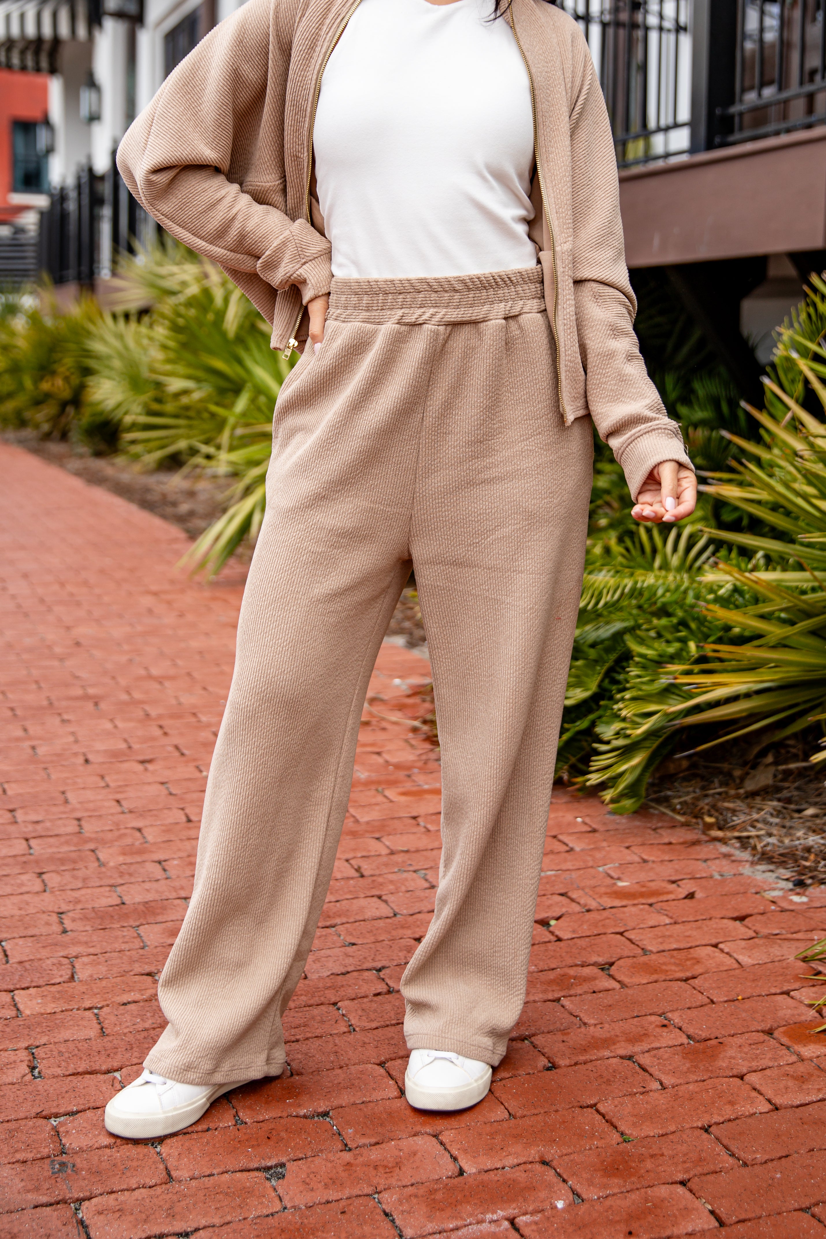 Person wearing a beige outfit with a white top on a brick path.