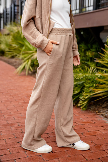 Person wearing beige cardigan and pants with white shoes on a brick path.