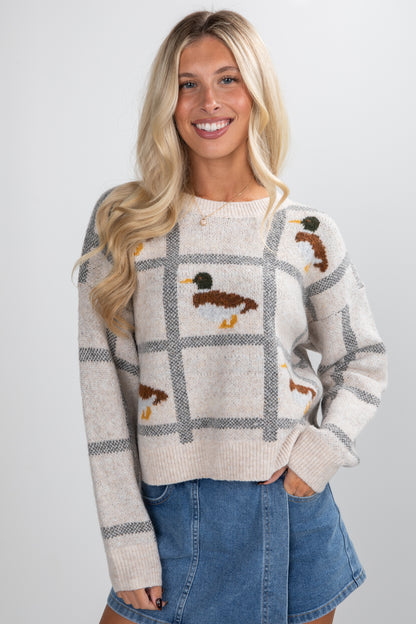 Woman wearing a patterned sweater with duck design on a plain background