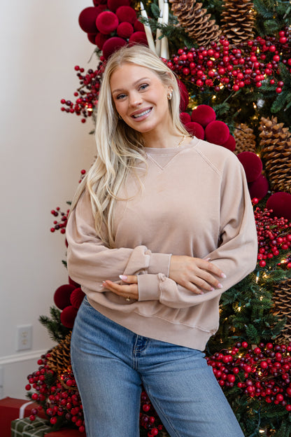 Woman in a beige sweater and blue jeans standing in front of a Christmas tree with red berries and pinecones.