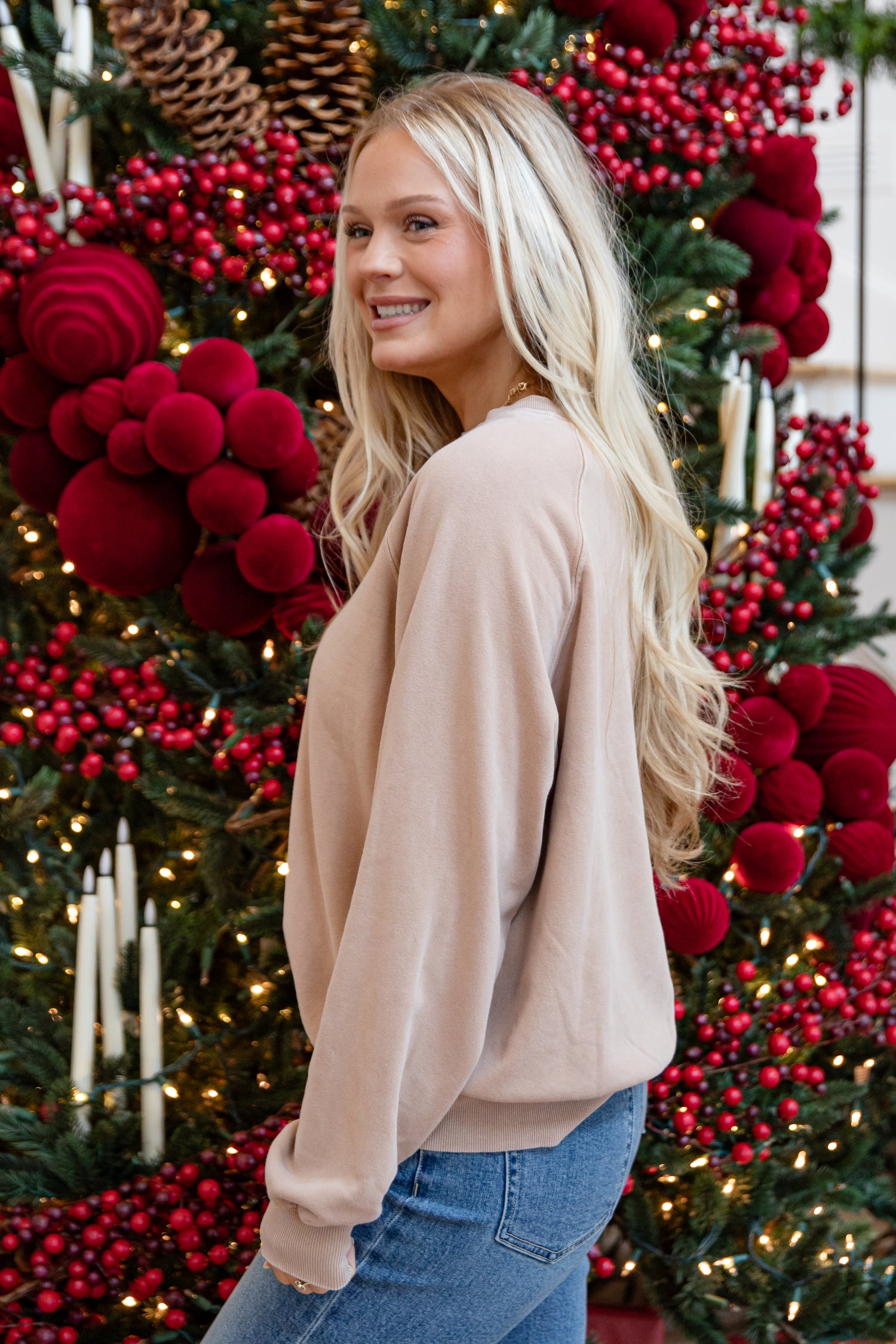 Woman standing in front of a Christmas tree decorated with red berries and lights.