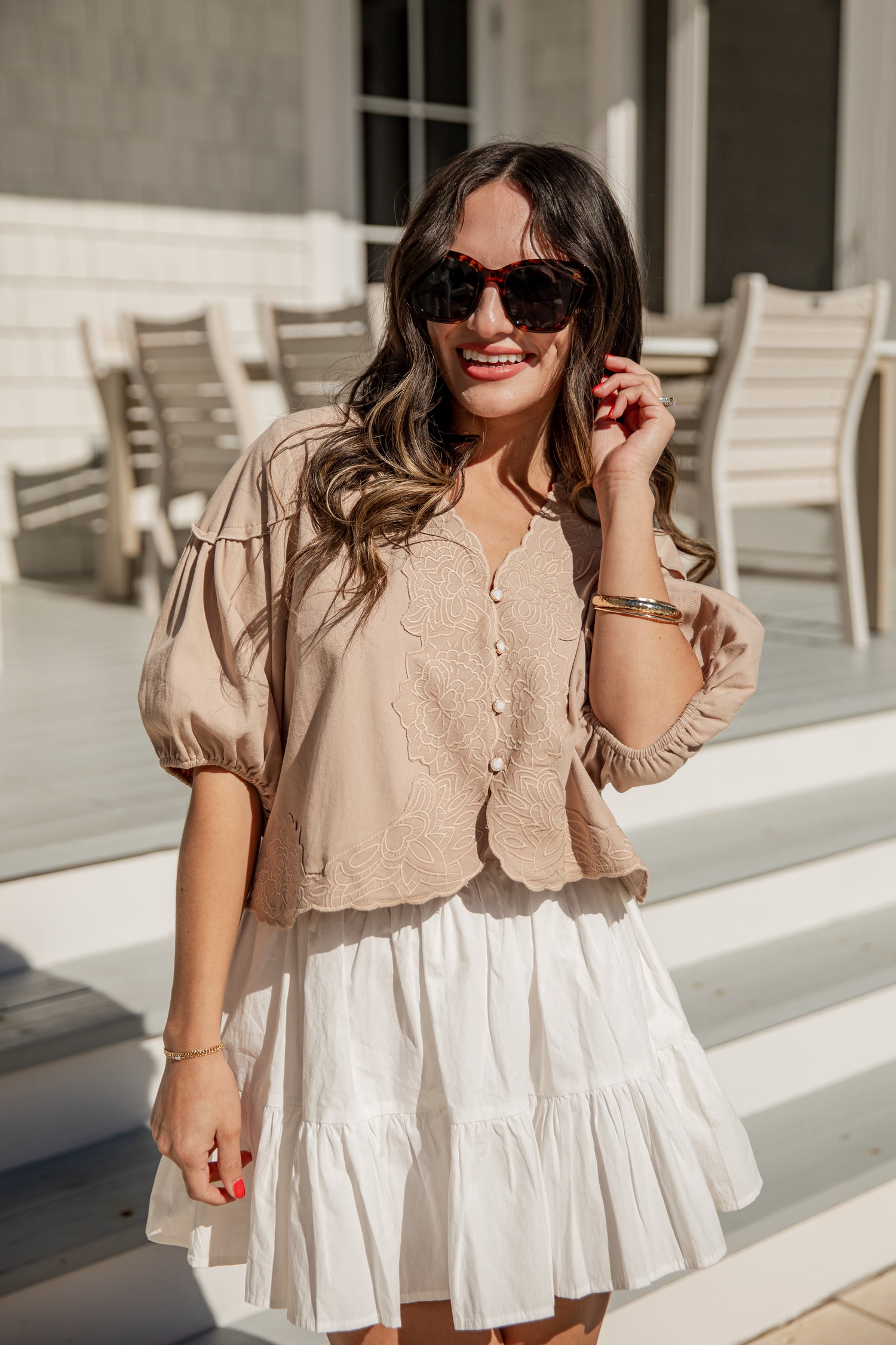 Woman wearing a beige blouse and white skirt outdoors.