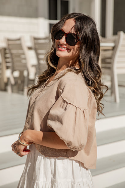 Woman wearing a beige blouse and sunglasses outdoors