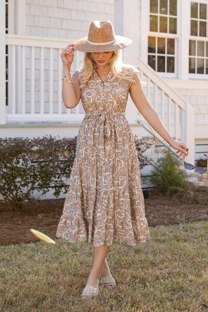 Woman in a floral dress and hat standing in front of a white house.