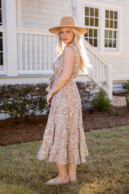 Woman in a patterned dress and hat standing in front of a house.