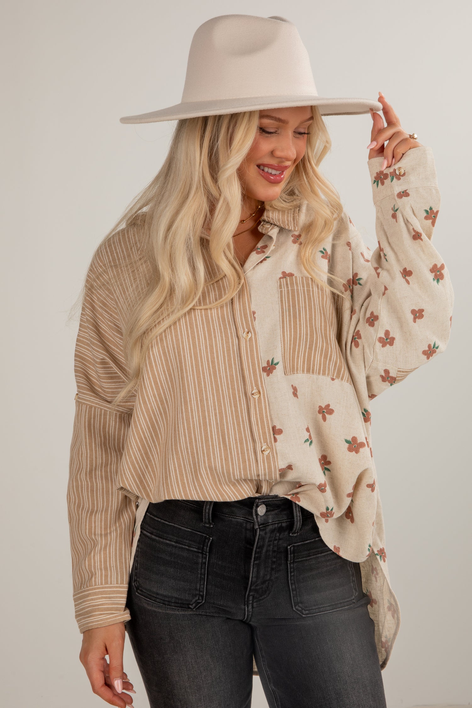 Woman wearing a beige hat, striped shirt, and floral blouse against a plain background