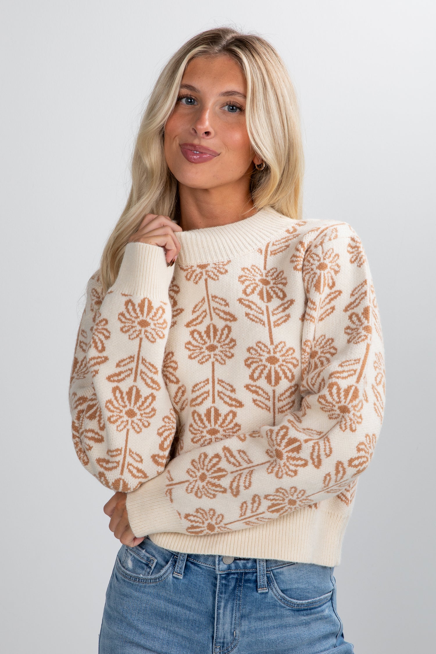 Woman wearing a beige sweater with floral patterns on a plain background