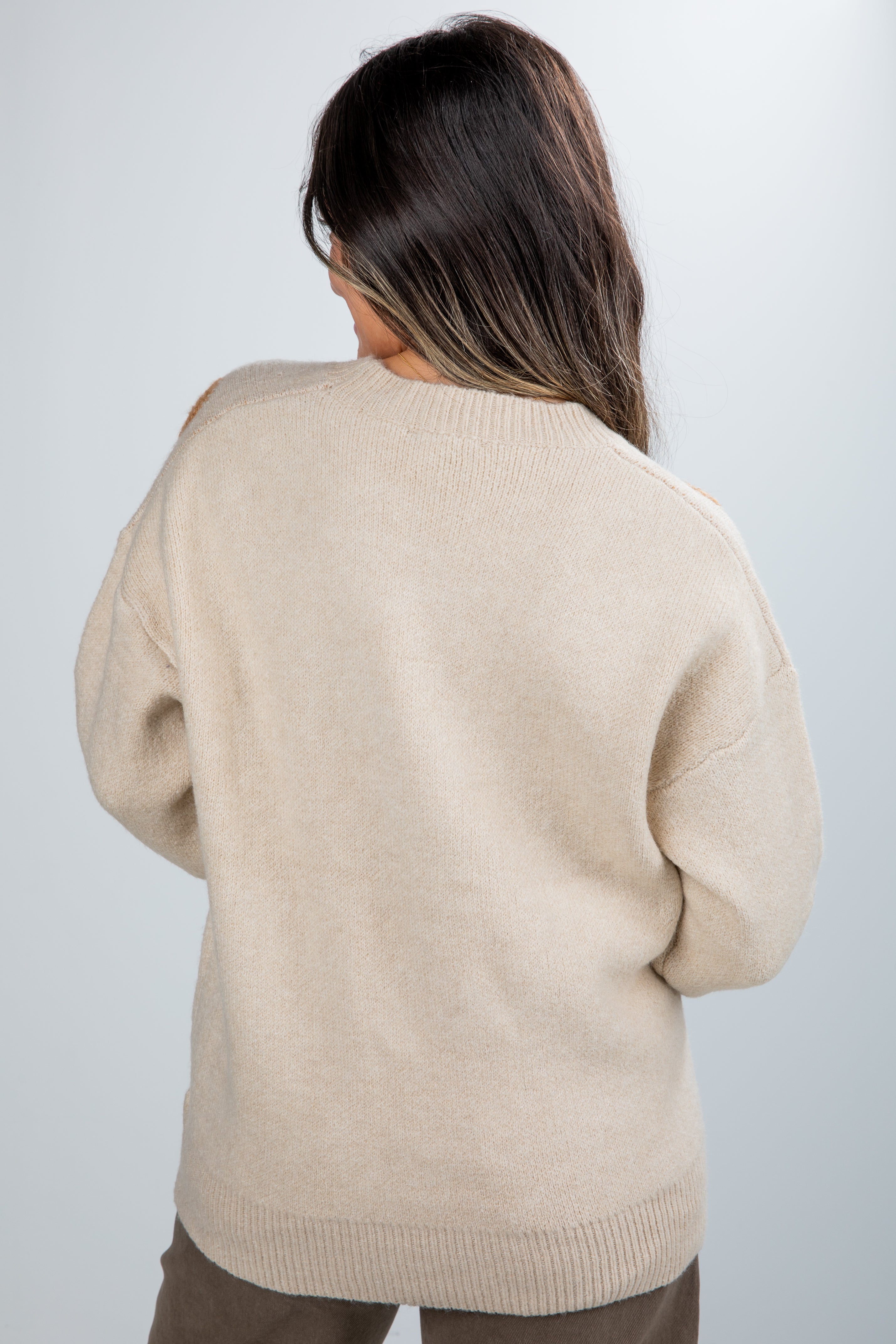 Person wearing a beige sweater against a plain background