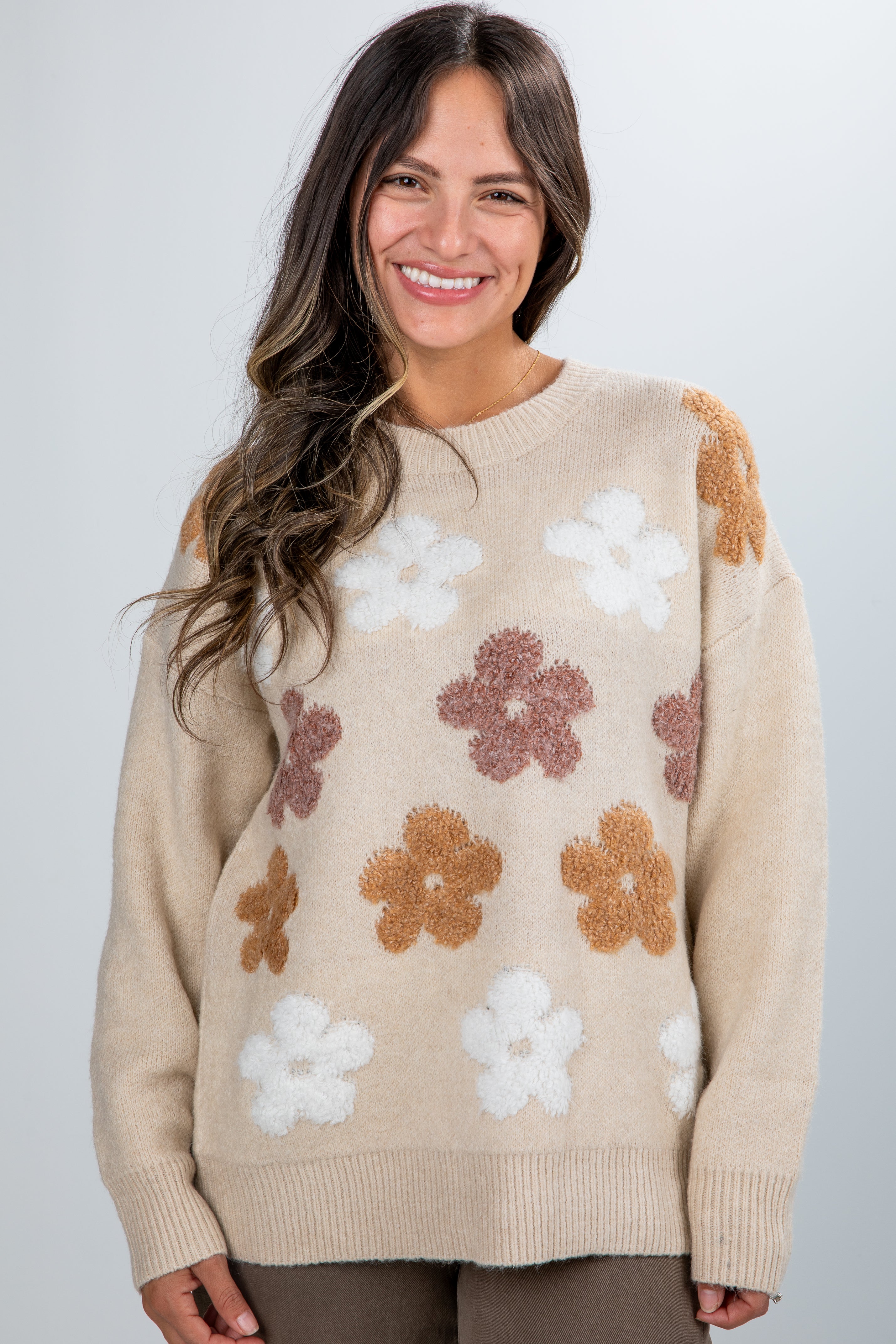 Woman wearing a beige sweater with floral patterns on a plain background