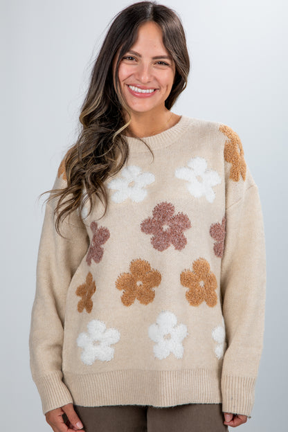 Woman wearing a beige sweater with floral patterns on a plain background