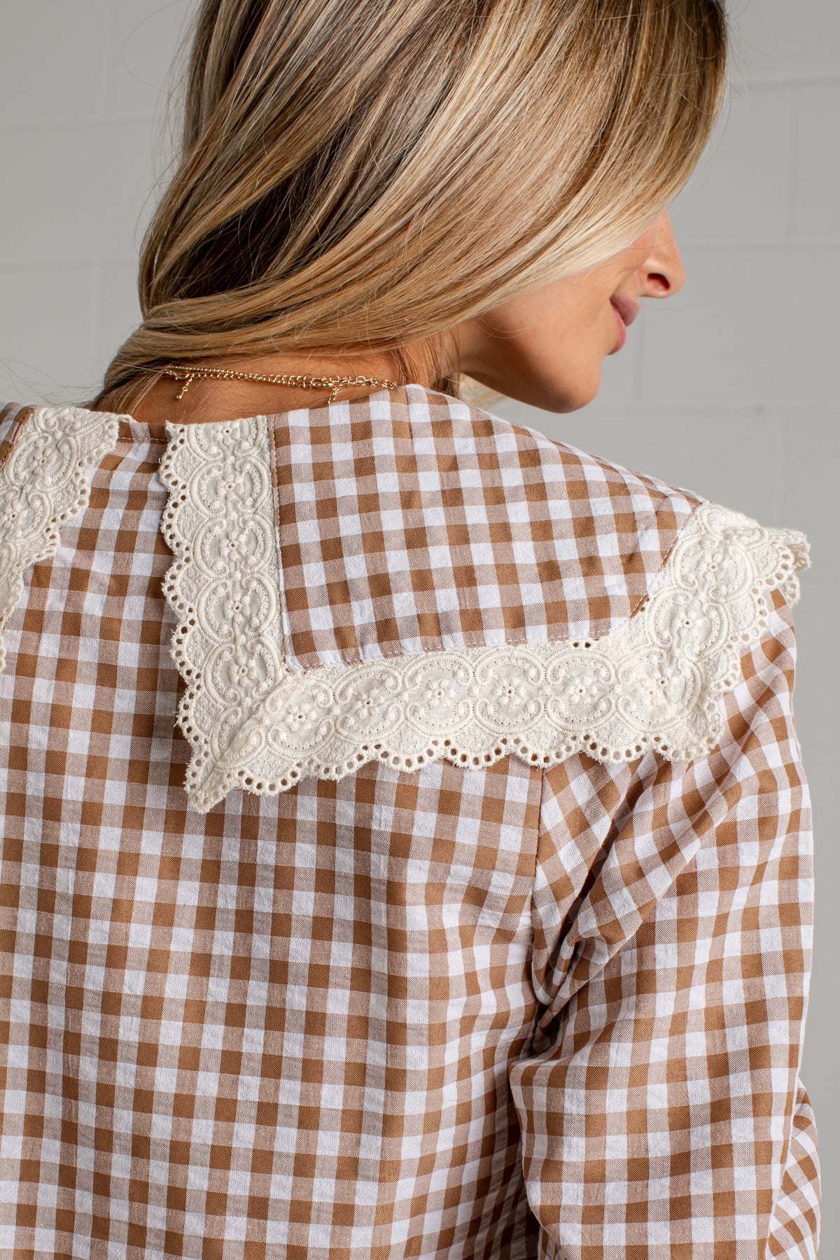 A close-up back view of a woman wearing a brown and white gingham shirt with a large white lace collar.