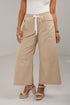 A model wearing beige wide-leg cropped pants with an elastic waistband and white drawstring, paired with a white top and beige platform sandals.