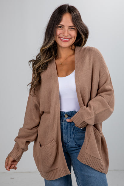 Woman wearing a brown cardigan over a white top and blue jeans on a white background