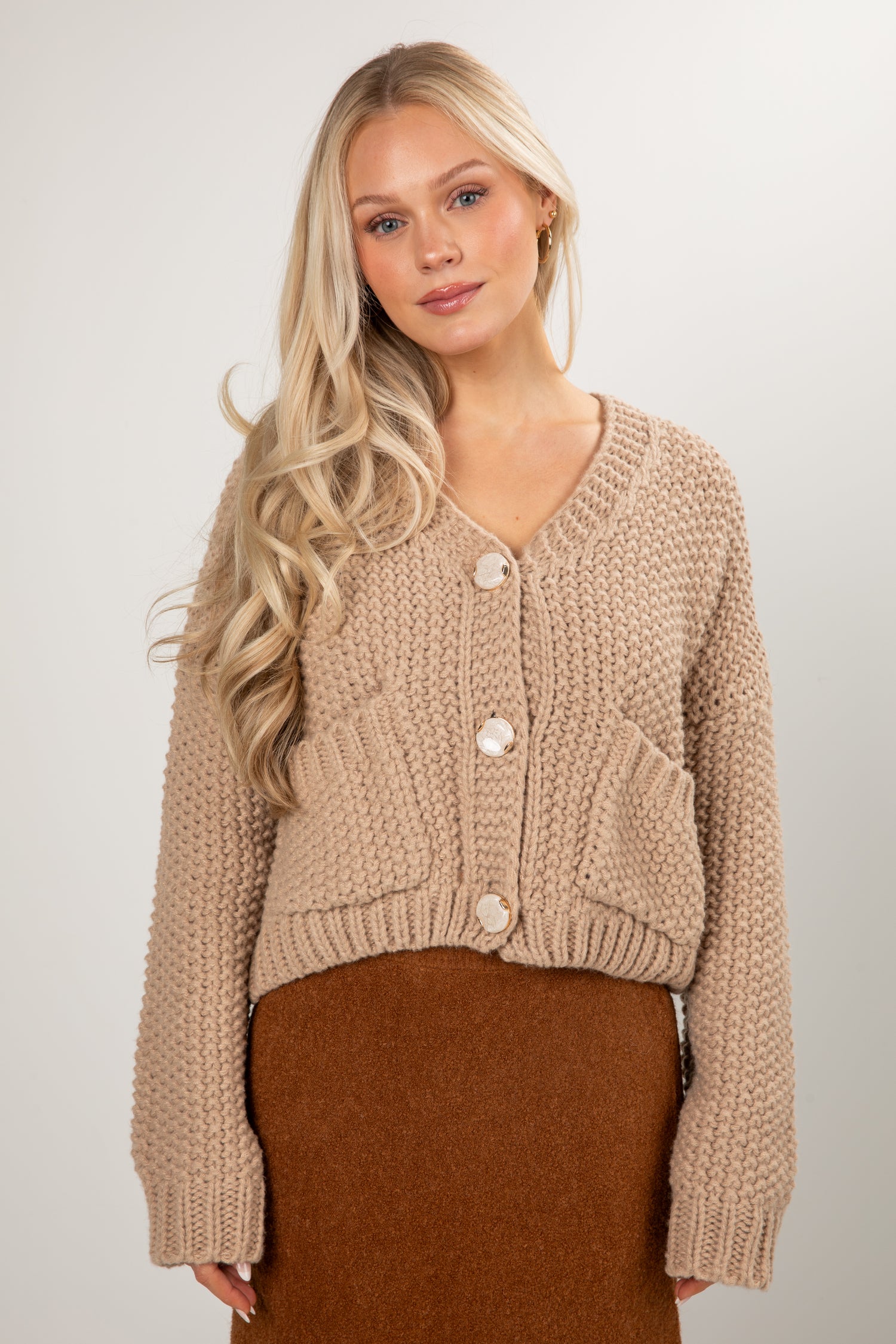 Woman wearing a beige knitted cardigan with a plain background