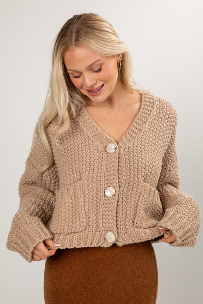 Woman wearing a beige knitted cardigan on a plain background