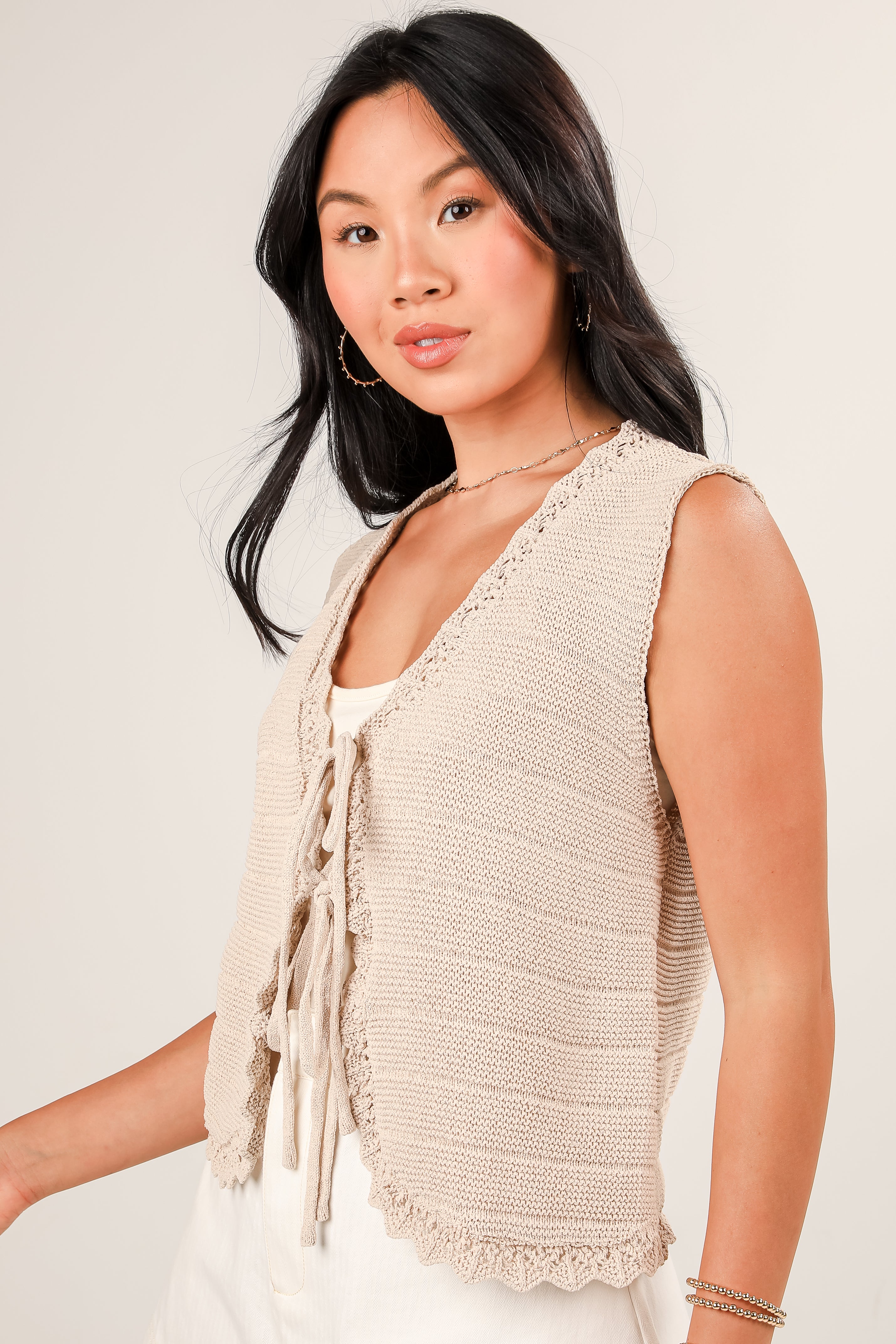 Woman wearing a beige knitted vest against a plain background