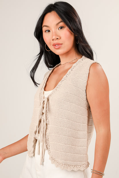 Woman wearing a beige knitted vest against a plain background