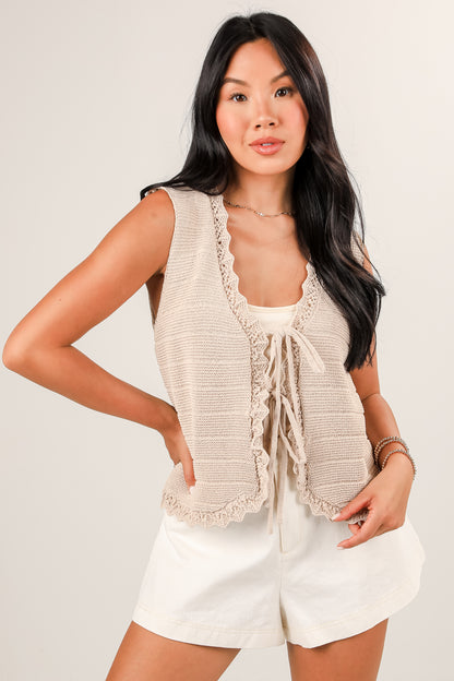 Woman wearing a beige sleeveless top with lace details and white shorts on a plain background