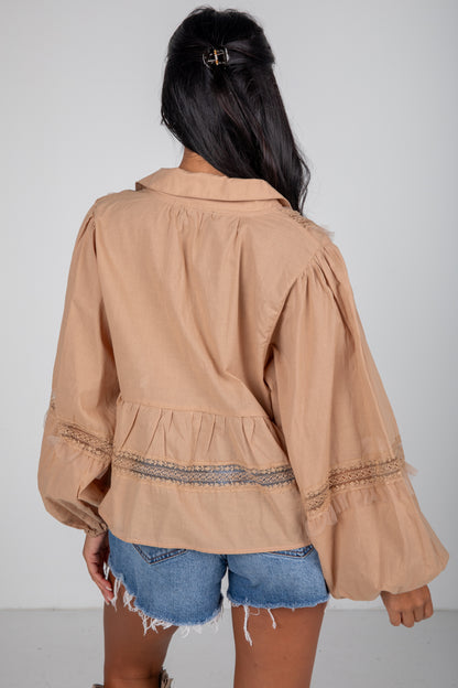 Person wearing a beige jacket with ruffled sleeves on a plain background