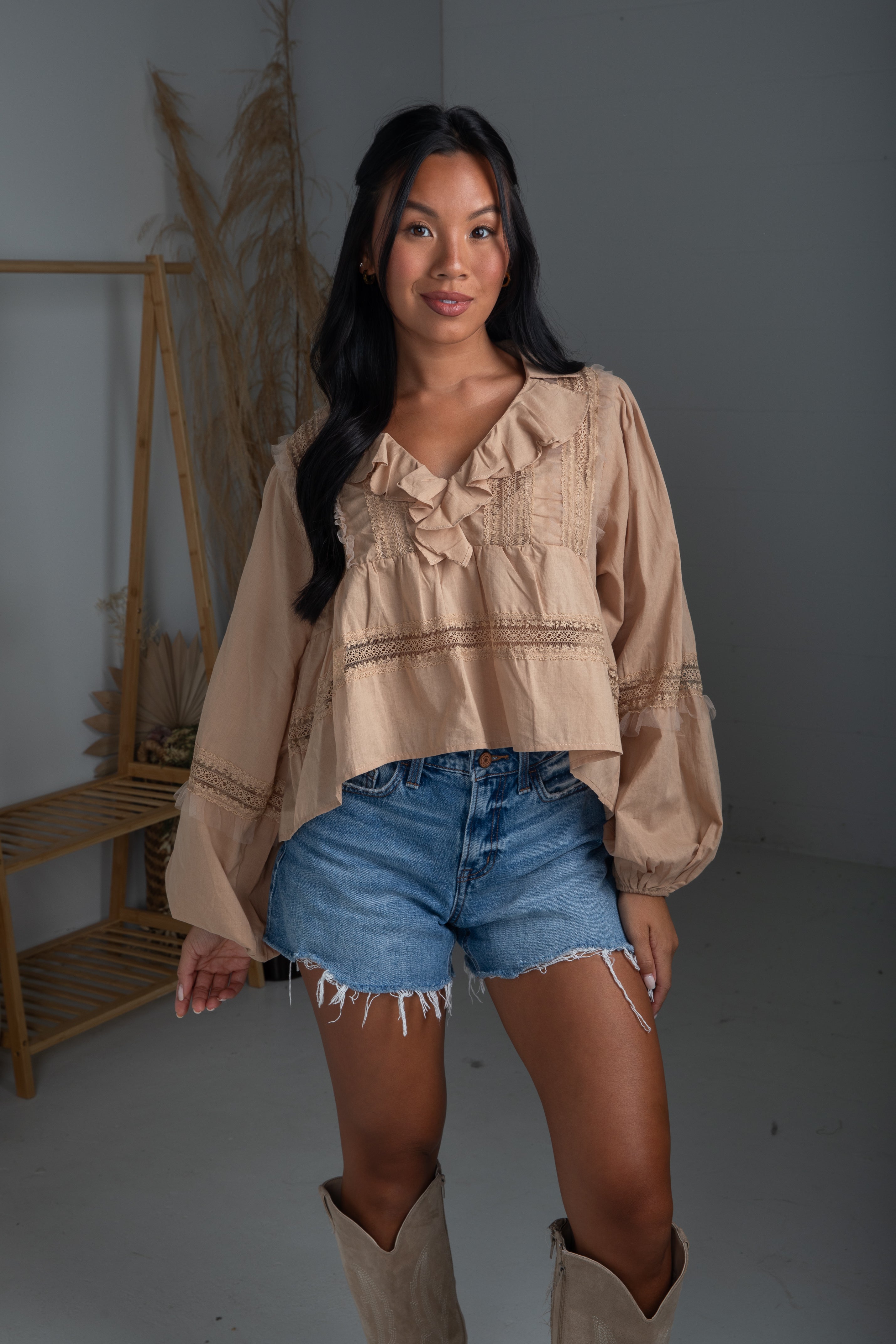 Woman wearing a beige blouse and denim shorts with boots in a minimalistic setting