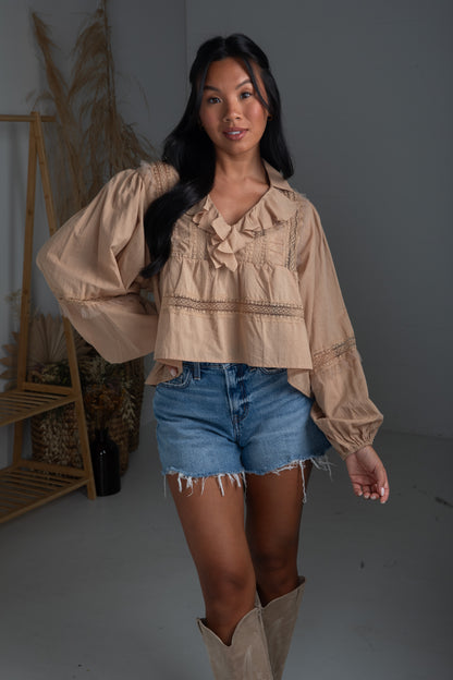 Woman wearing a beige blouse, denim shorts, and brown boots in a minimalistic setting.