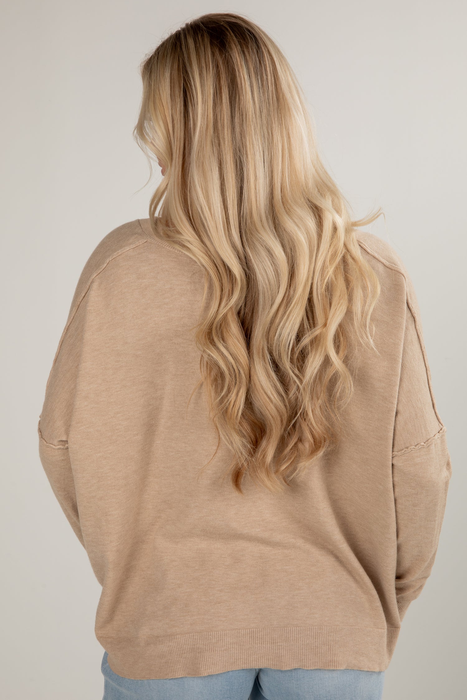 Person wearing a beige sweater with long blonde hair on a plain background