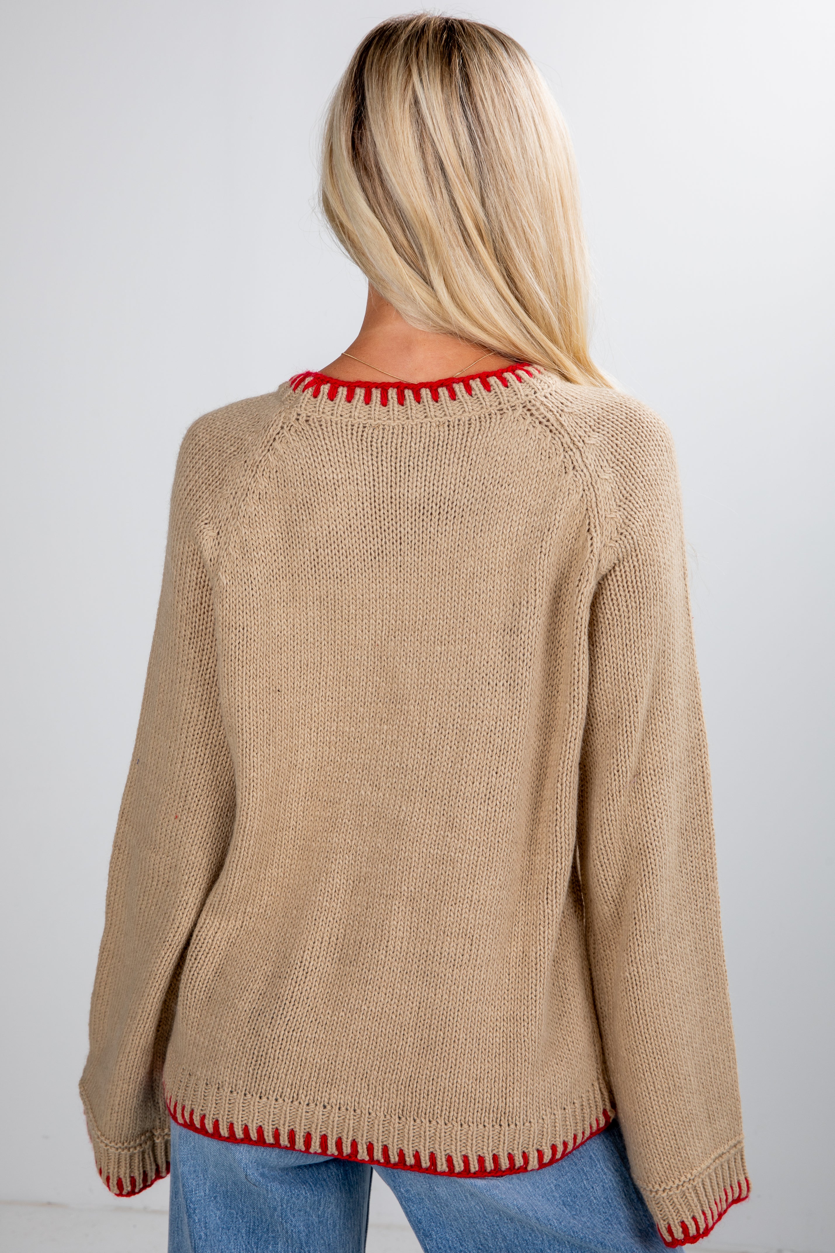 Person wearing a beige sweater with red trim on a plain background